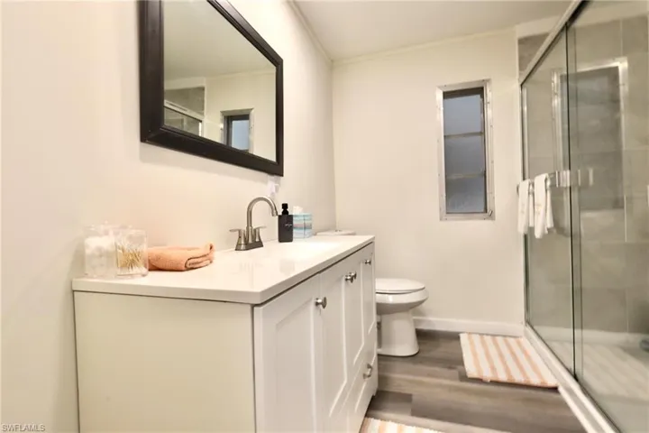 Bathroom with hardwood / wood-style flooring, a shower with door, crown molding, vanity, and toilet