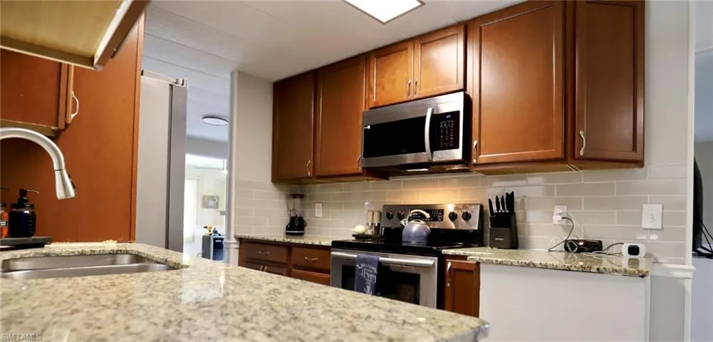 Kitchen with appliances with stainless steel finishes, backsplash, sink, and light stone counters