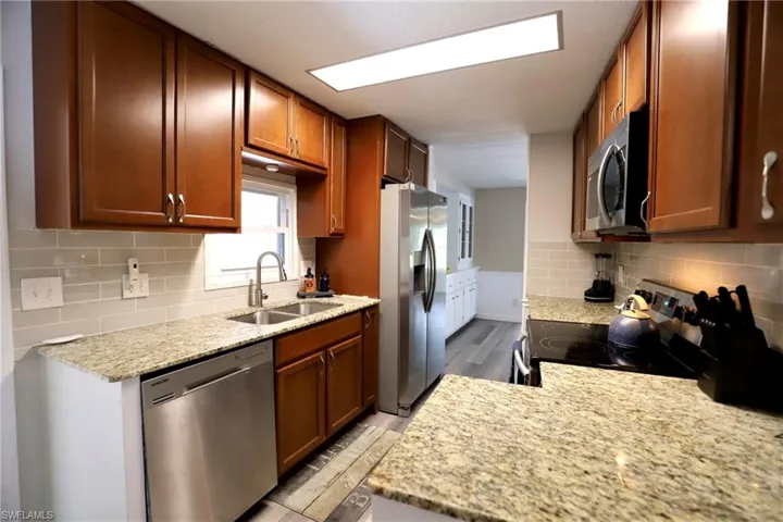 Kitchen with light stone counters, tasteful backsplash, stainless steel appliances, light hardwood / wood-style flooring, and sink