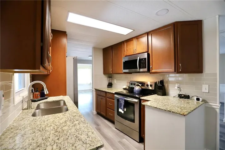 Kitchen featuring light stone counters, sink, tasteful backsplash, stainless steel appliances, and light wood-type flooring