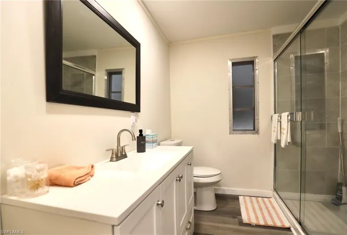 Bathroom featuring vanity, crown molding, wood-type flooring, toilet, and an enclosed shower