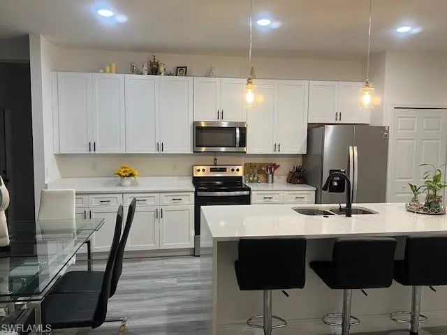 Kitchen with decorative light fixtures, stainless steel appliances, light stone counters, and white cabinetry