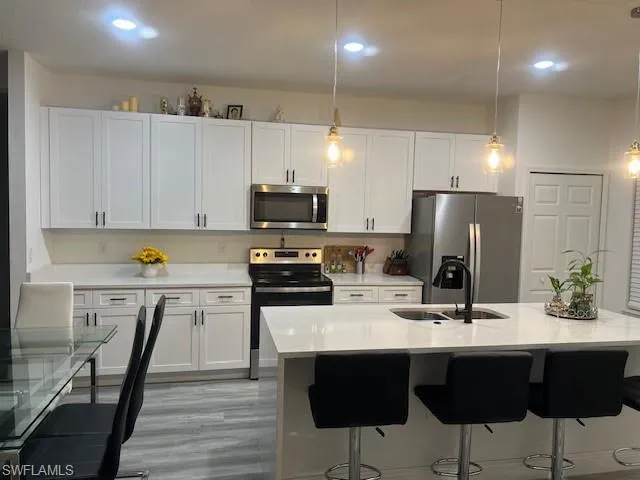 Kitchen with decorative light fixtures, light stone counters, stainless steel appliances, a kitchen bar, and white cabinets