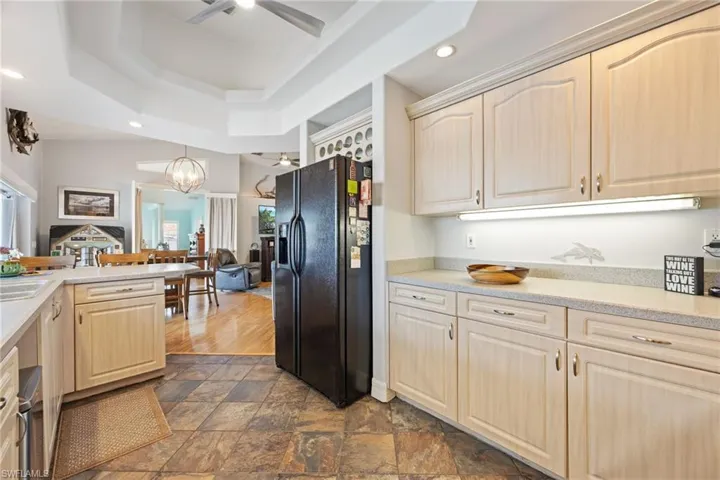Kitchen featuring light wood finish cabinetry, black fridge, stone finish flooring, ceiling fan, and light stone counters