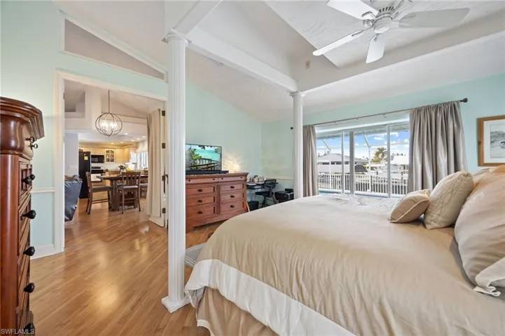 Bedroom with access to outside, wood finished floors, vaulted ceiling, a chandelier, and ceiling fan