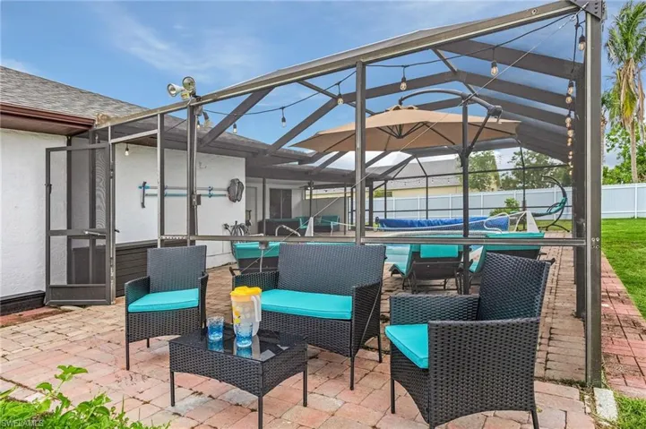 Paved patio area featuring a screened enclosure, string lighting, and an in-ground pool