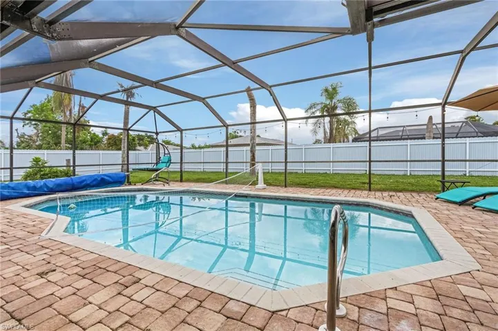Screened-in outdoor pool area featuring a paver patio surround, clear blue water, and a perimeter safety fence
