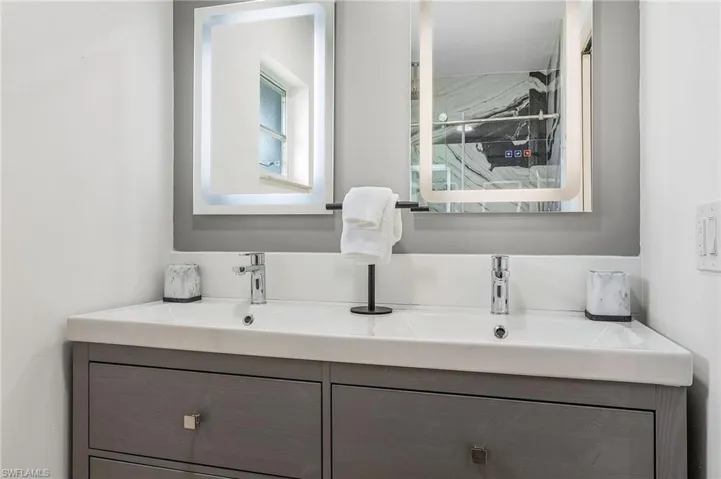 Dual vanity with integrated sinks, contemporary chrome faucets, light gray cabinetry, and backlit mirrors