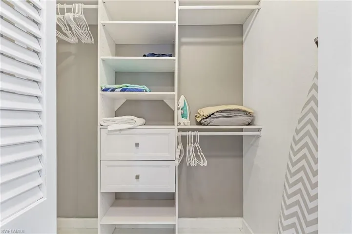 Custom closet system featuring white shelving units, two integrated drawers with brushed nickel hardware, and multiple hanging rods
