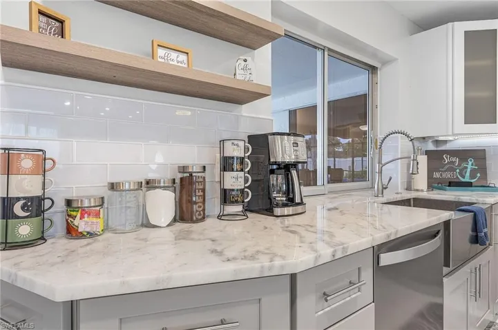 Kitchen countertop featuring a light-toned stone surface with grey veining, a stainless steel sink with a gooseneck faucet, light grey base cabinetry with chrome hardware, and a white subway tile backsplash