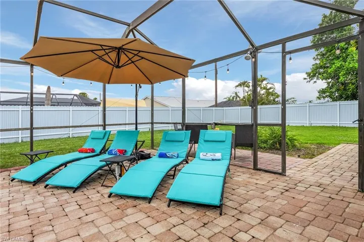 Screened outdoor living space featuring paver flooring, string lighting, and direct access to a grassy yard with a privacy fence