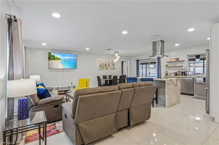Open-concept living space featuring high-gloss tile flooring, recessed lighting, and a contemporary kitchen with a large stone waterfall island and stainless steel appliances