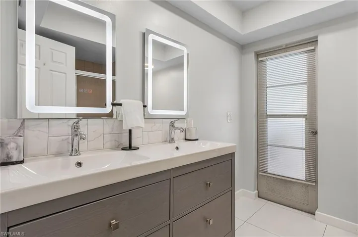 Bathroom vanity featuring dual under-mount sinks with chrome faucets, a white countertop, and gray cabinetry