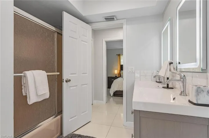 Bathroom vanity featuring dual sinks with chrome fixtures, integrated mirrors with backlighting, and a subway tile backsplash