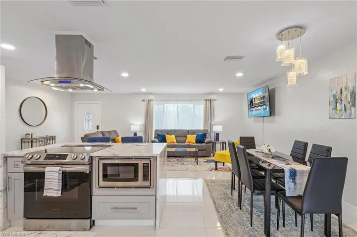 Open-concept living space featuring a kitchen island with built-in range and microwave, a dining area with a contemporary chandelier, recessed lighting, and a front entry door with decorative glass