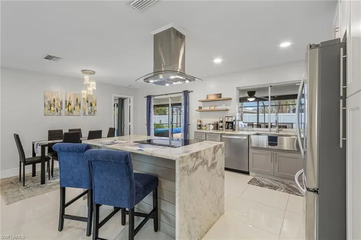 Modern kitchen featuring a waterfall island, built-in cooktop, and stainless steel hood
