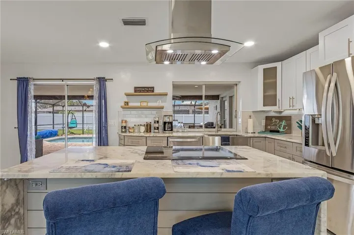 Modern kitchen featuring a large central island with an integrated cooktop, stone countertops, and a stainless steel range hood