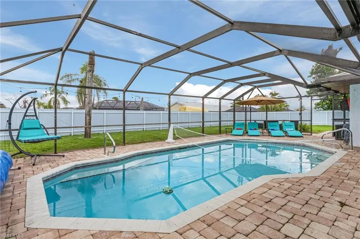Screened-in outdoor pool featuring a paver deck, white perimeter fencing, and surrounding green lawn