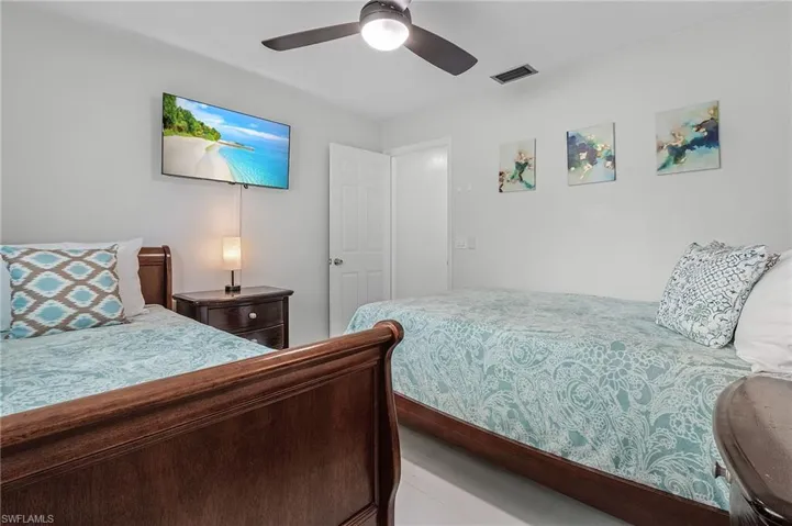Bright room featuring wood-finish bed frames, a mounted flat-screen television, a ceiling fan, and white walls