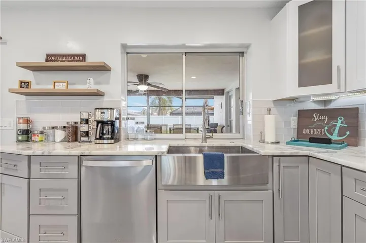 Modern kitchen featuring gray shaker-style cabinetry, a stainless steel farmhouse sink, and light-toned countertops