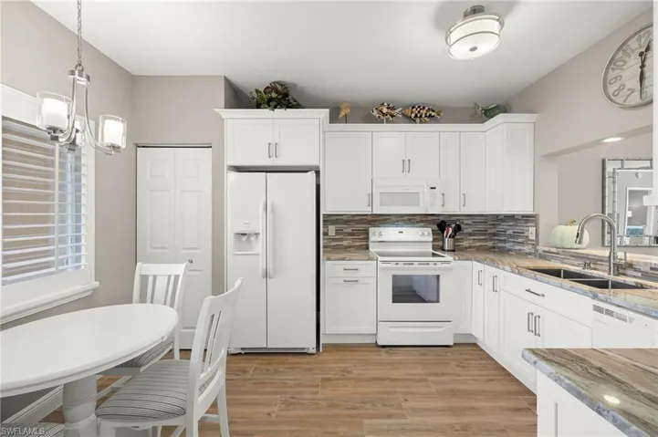 Kitchen with white cabinetry, light hardwood / wood-style floors, decorative light fixtures, sink, and white appliances