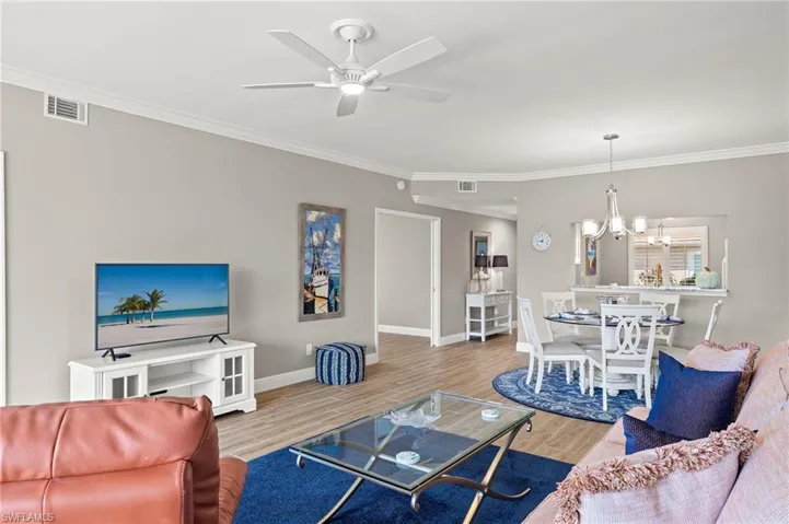 Living room with crown molding, ceiling fan with notable chandelier, and hardwood / wood-style floors
