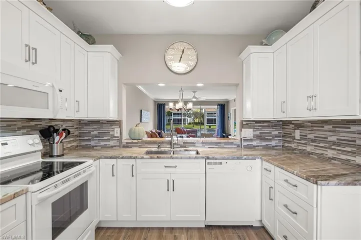 Kitchen with white appliances, sink, white cabinetry, light hardwood / wood-style floors, and a notable chandelier