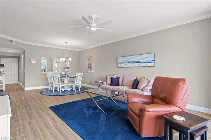 Living room with ornamental molding, light hardwood / wood-style flooring, and ceiling fan with notable chandelier