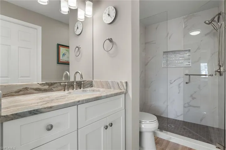 Bathroom with vanity, a shower with shower door, toilet, and wood-type flooring