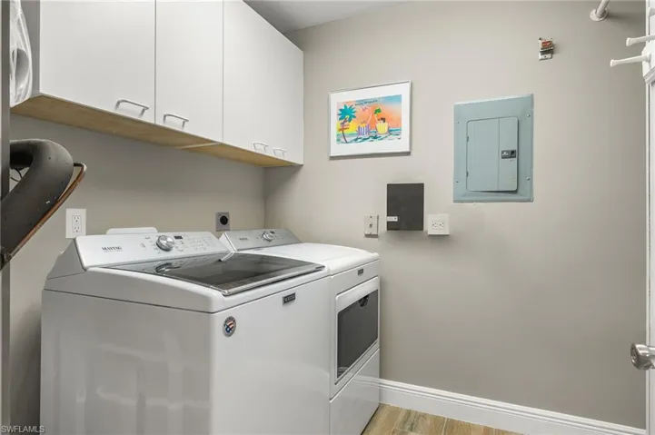 Washroom with cabinets, electric panel, separate washer and dryer, and light hardwood / wood-style floors