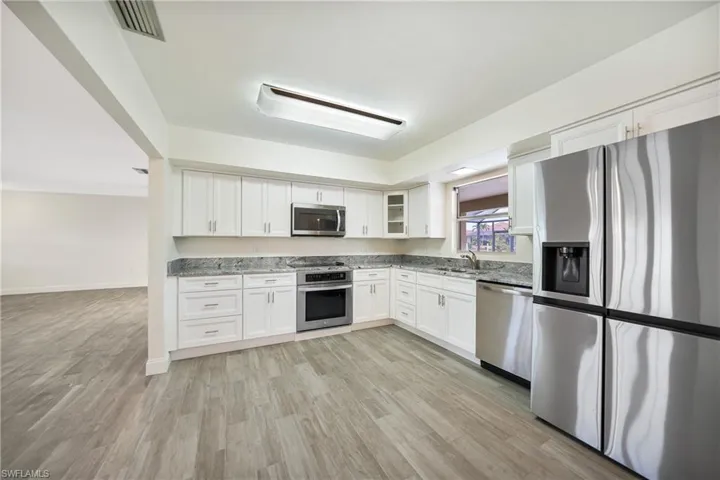 Kitchen featuring sink, light hardwood / wood-style flooring, stainless steel appliances, light stone counters, and white cabinets