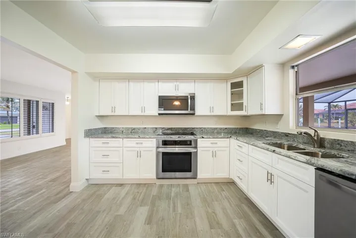 Kitchen featuring appliances with stainless steel finishes, stone countertops, sink, white cabinets, and light hardwood / wood-style floors
