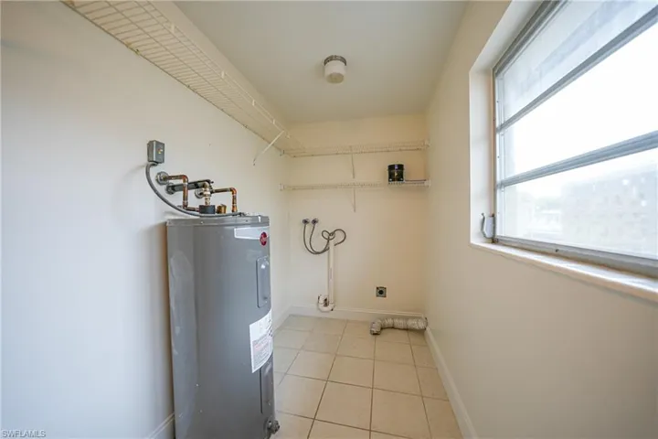 Washroom with water heater, electric dryer hookup, and light tile patterned floors