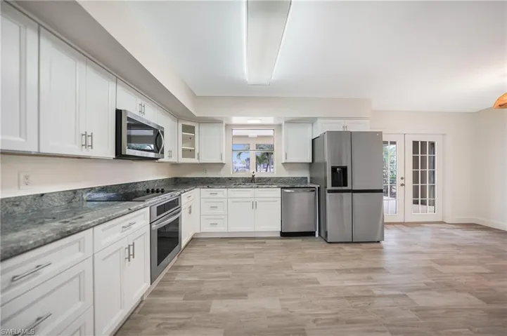 Kitchen featuring dark stone countertops, white cabinets, stainless steel appliances, light wood-type flooring, and french doors