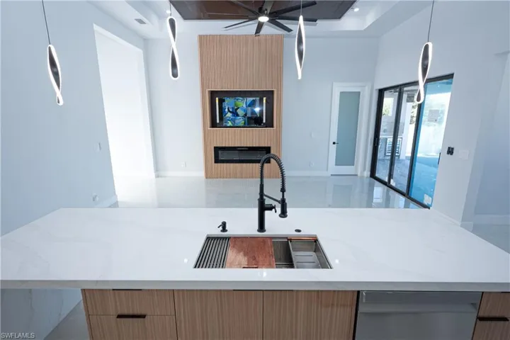 Kitchen featuring baseboards, light stone counters, open floor plan, modern cabinets, and a sink
