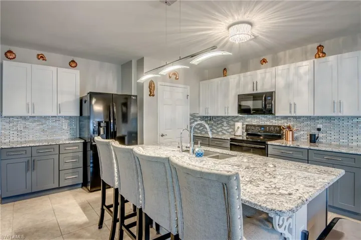 Kitchen with a kitchen island with sink, pendant lighting, black appliances, and sink