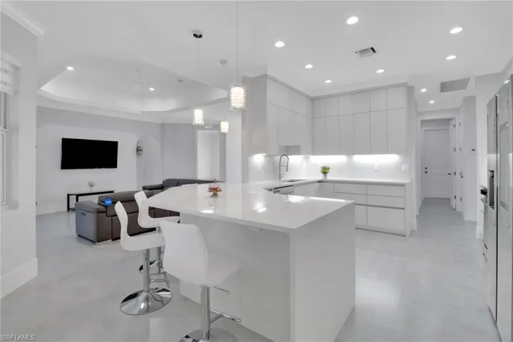Kitchen featuring a kitchen bar, sink, white cabinetry, crown molding, and decorative light fixtures