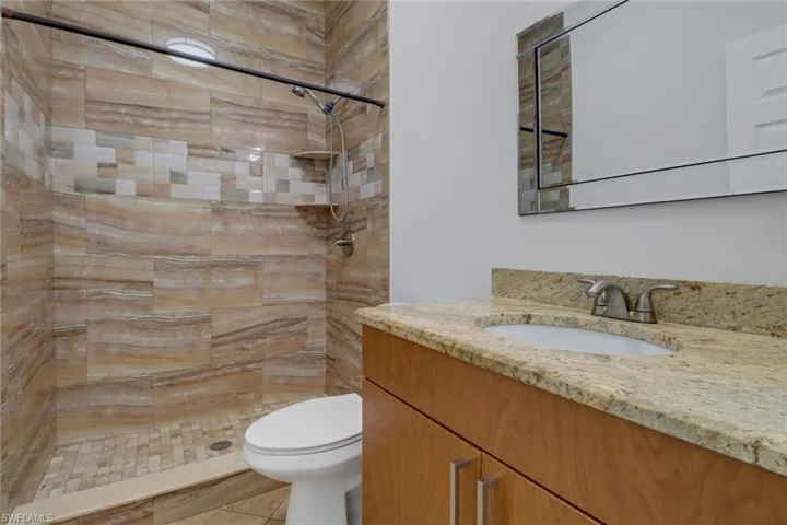 Bathroom featuring vanity, toilet, and tiled shower