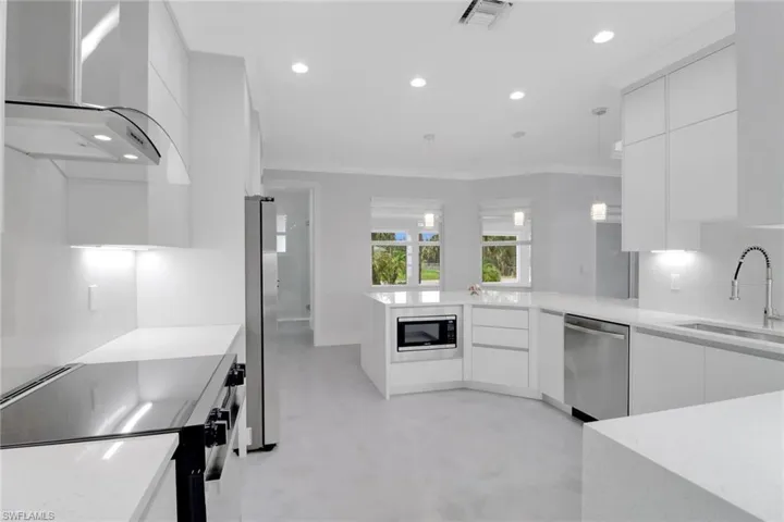 Kitchen featuring wall chimney range hood, sink, white cabinetry, hanging light fixtures, and stainless steel appliances