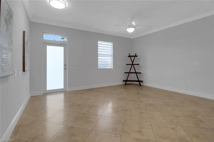Empty room featuring crown molding, ceiling fan, and light tile patterned floors