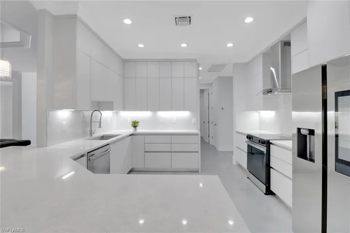 Kitchen featuring sink, white cabinetry, kitchen peninsula, stainless steel appliances, and wall chimney range hood