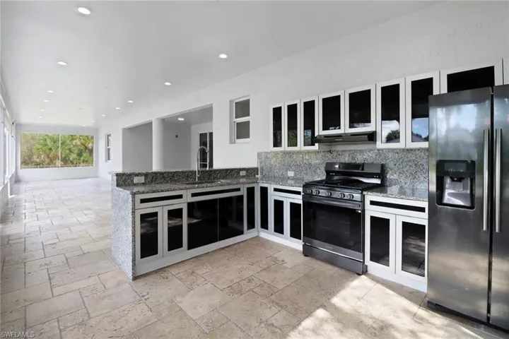 Kitchen with appliances with stainless steel finishes, stone countertops, sink, backsplash, and kitchen peninsula