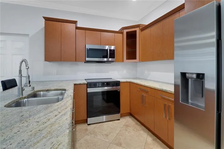 Kitchen with sink, light stone counters, crown molding, light tile patterned floors, and appliances with stainless steel finishes
