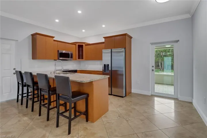 Kitchen featuring sink, crown molding, appliances with stainless steel finishes, kitchen peninsula, and light stone countertops