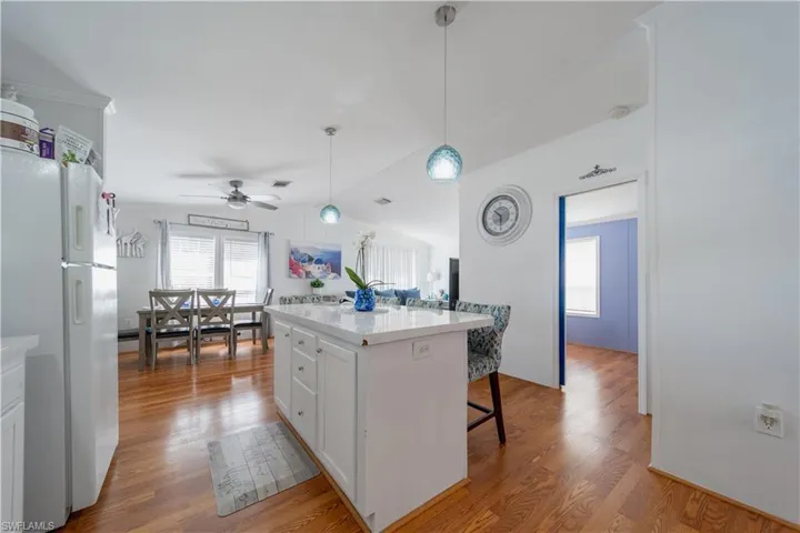 Kitchen featuring freestanding refrigerator, wood finished floors, white cabinetry, a breakfast bar area, and light countertops