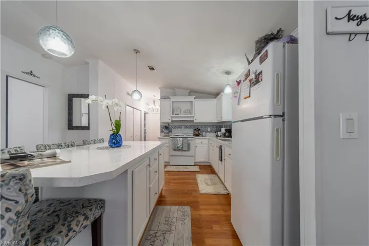 Kitchen featuring white appliances, open shelves, white cabinetry, light wood finished floors, and pendant lighting