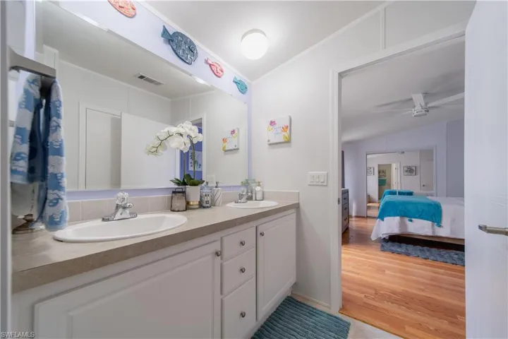 Ensuite bathroom with double vanity, ornamental molding, ceiling fan, and wood finished floors