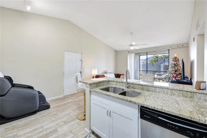 Kitchen with light stone counters, stainless steel dishwasher, sinklight wood-style tile floors, and white shaker cabinets