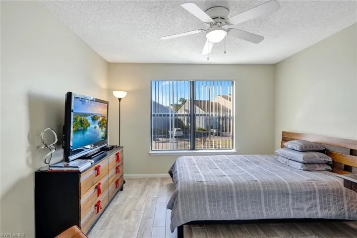 Bedroom with ceiling fan, a textured ceiling, and light wood-style tile floors