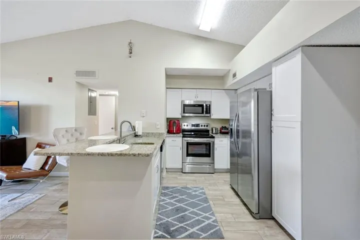 Kitchen with kitchen peninsula, light wood-style tile floors, stainless steel appliances, white shaker cabinets, and lofted ceiling